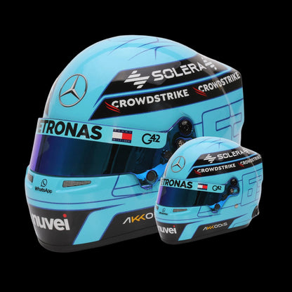 A mini replica helmet of George Russell, Mercedes F1 driver, in a 1:2 scale, featuring a light blue color with black and white accents, along with sponsor logos such as 'Astronas' and 'Crowdstrike'.